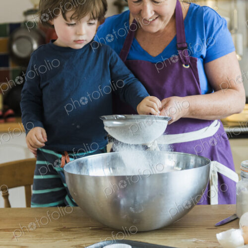 A woman and a child cooking at a kitchen table, making fairy cakes.