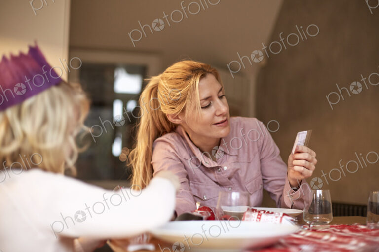 A woman and a child seated at a kitchen table sharing a cracker joke.