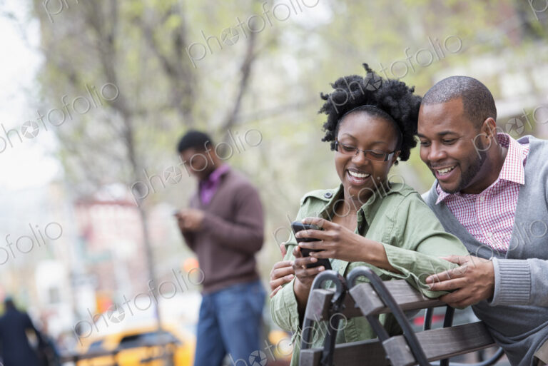 A woman and a man on a bench checking her phone.