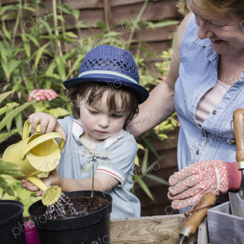 A woman and a young child water new seeds planted in a pot.