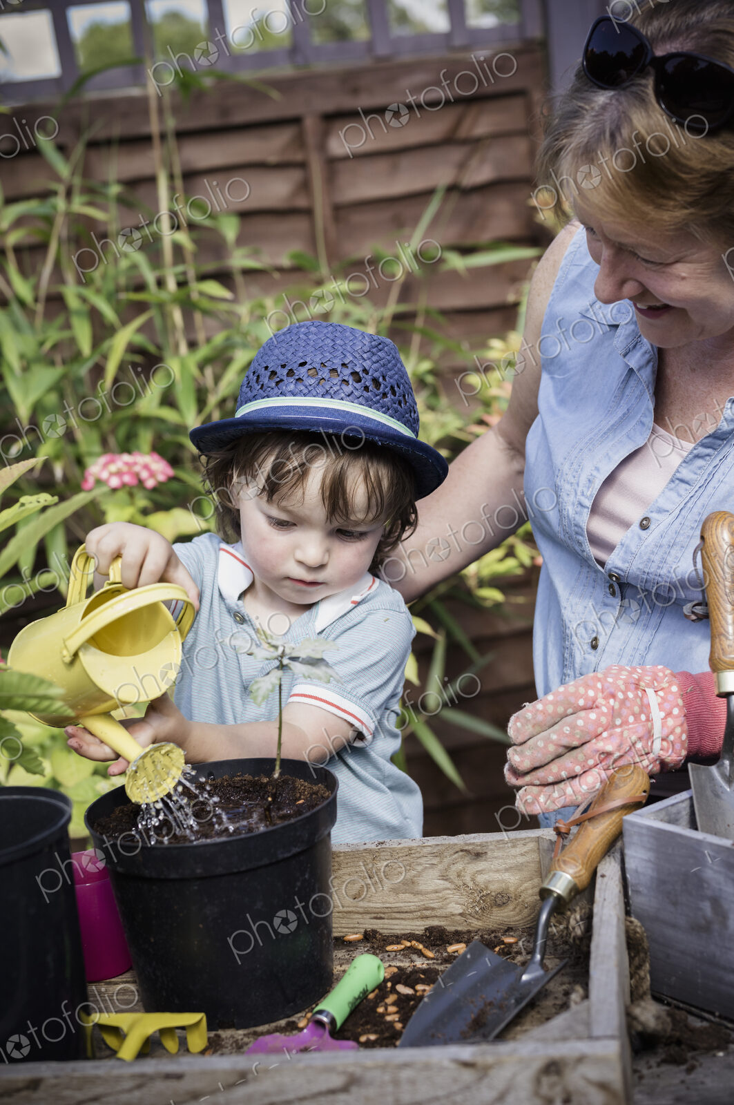 A woman and a young child water new seeds planted in a pot.