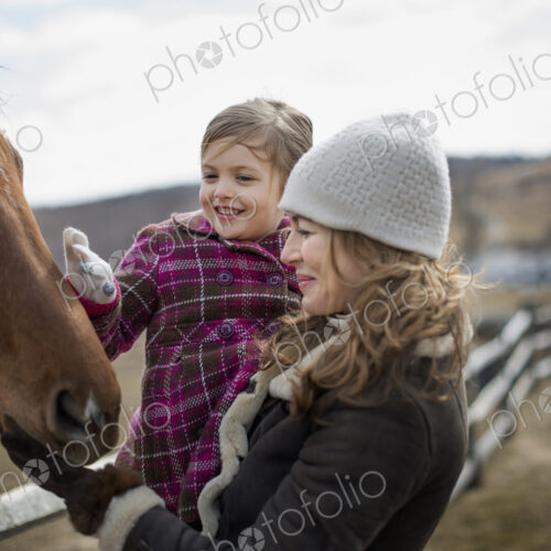 A woman and child patting a horse in a paddock on a farm. A woman and child patting a horse in a paddock on a farm.