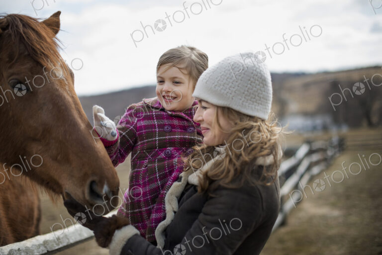 A woman and child patting a horse in a paddock on a farm.