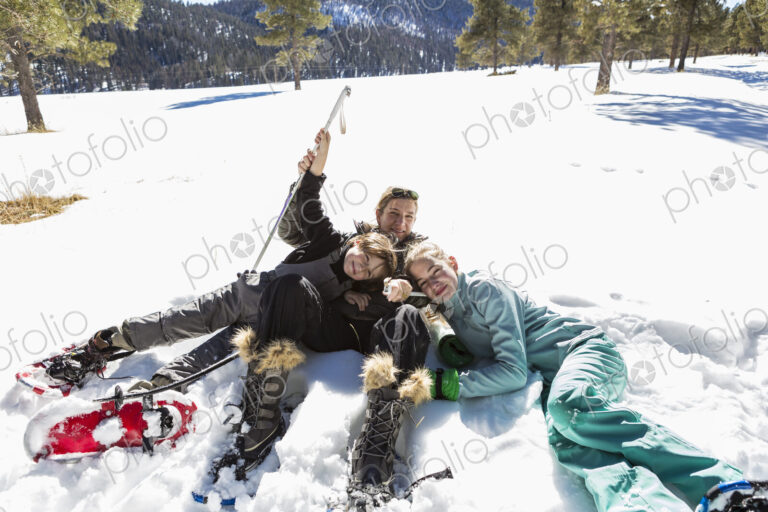 A woman and her two children lying in the snow in snow shoes and ski gear.