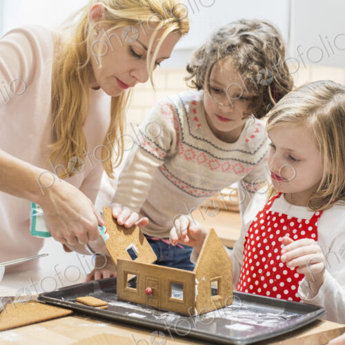 A woman and three children creating a baked gingerbread house.