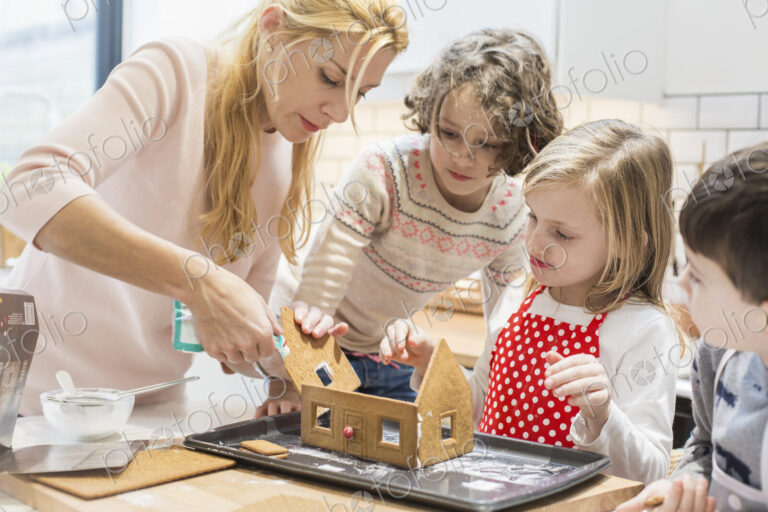 A woman and three children creating a baked gingerbread house.