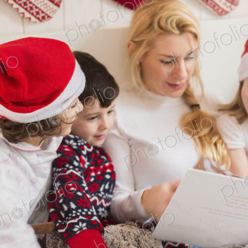 A woman and three children using a laptop computer sitting in a row in bed on…