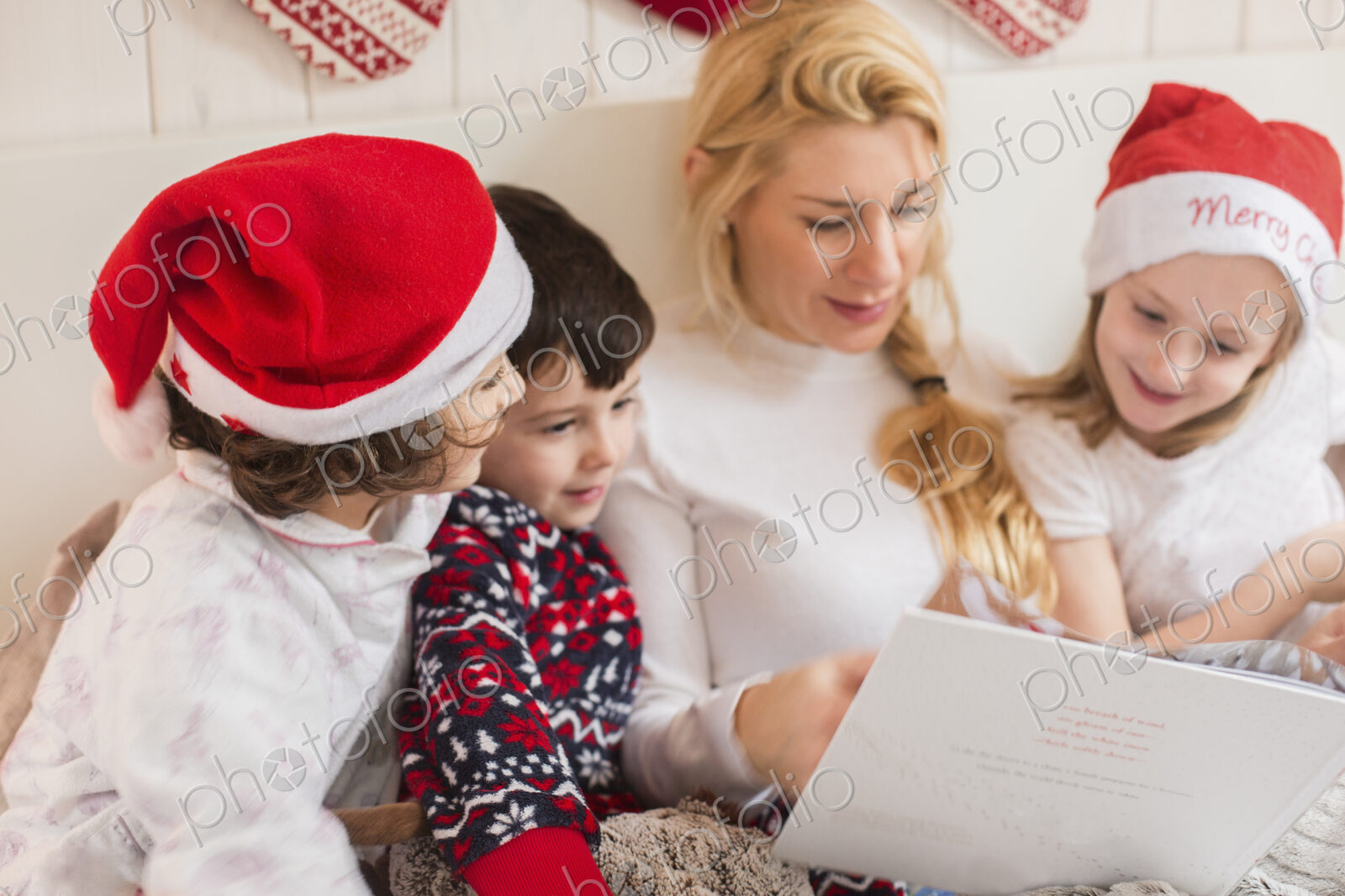 A woman and three children using a laptop computer sitting in a row in bed on…