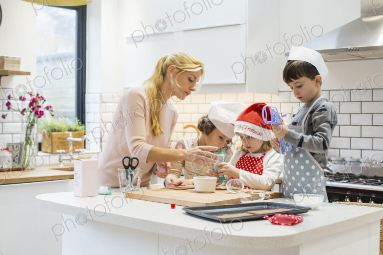 A woman and three children working together, making a gingerbread house, and icing the…
