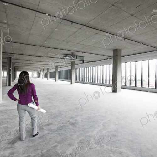 A woman architect holding architectural drawings looking out over a new raw business…