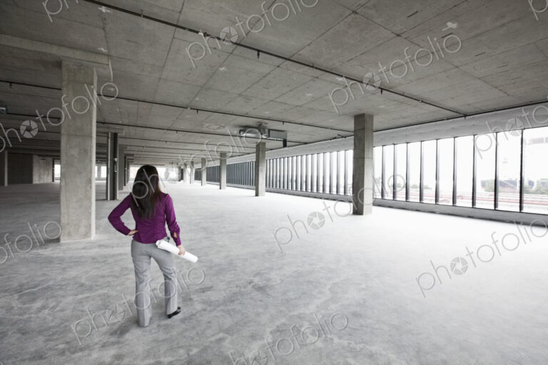 A woman architect holding architectural drawings looking out over a new raw business…