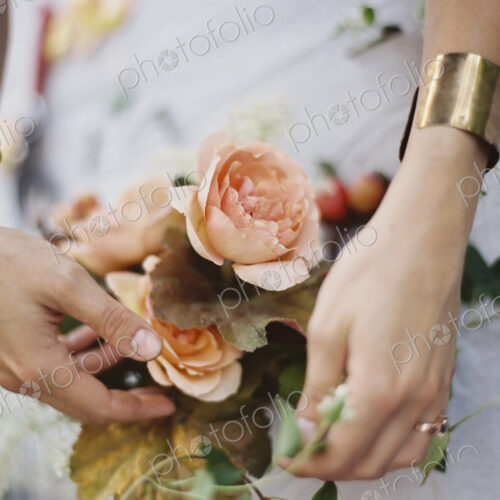 A woman arranging fresh flowers on a tabletop covered with a white cloth. Peach… A woman arranging fresh flowers on a tabletop covered with a white cloth. Peach…