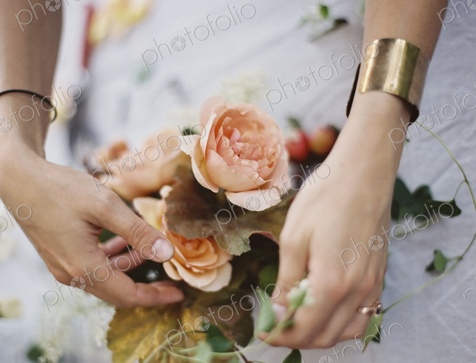 A woman arranging fresh flowers on a tabletop covered with a white cloth. Peach…