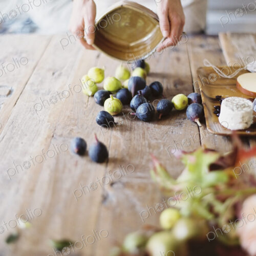 A woman at a domestic kitchen table arranging figs and cheese for a meal A woman at a domestic kitchen table arranging figs and cheese for a meal