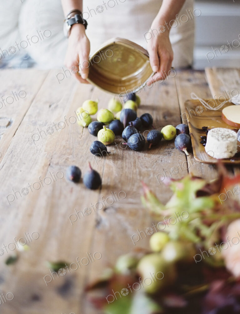 A woman at a domestic kitchen table arranging figs and cheese for a meal