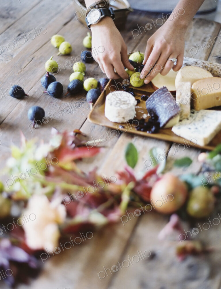 A woman at a domestic kitchen table. Arranging fresh fruit, black and green figs on a…