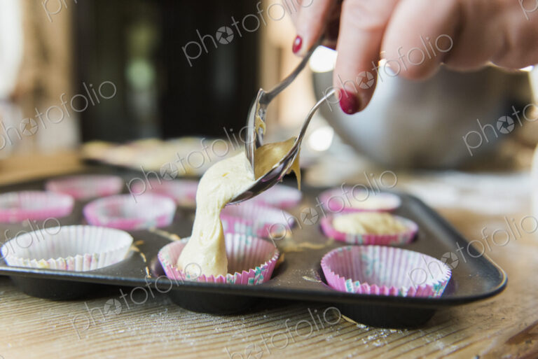A woman at a kitchen table baking fairy cakes.