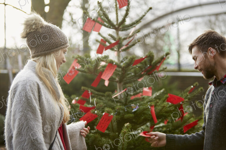 A woman by a Christmas tree reading the red labels on branches.