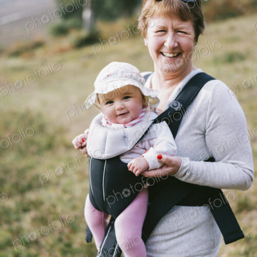 A woman carrying a baby in a baby carrier, outdoors.