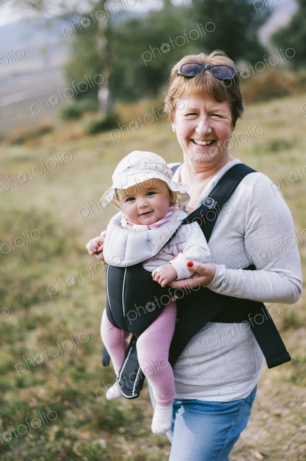 A woman carrying a baby in a baby carrier, outdoors.