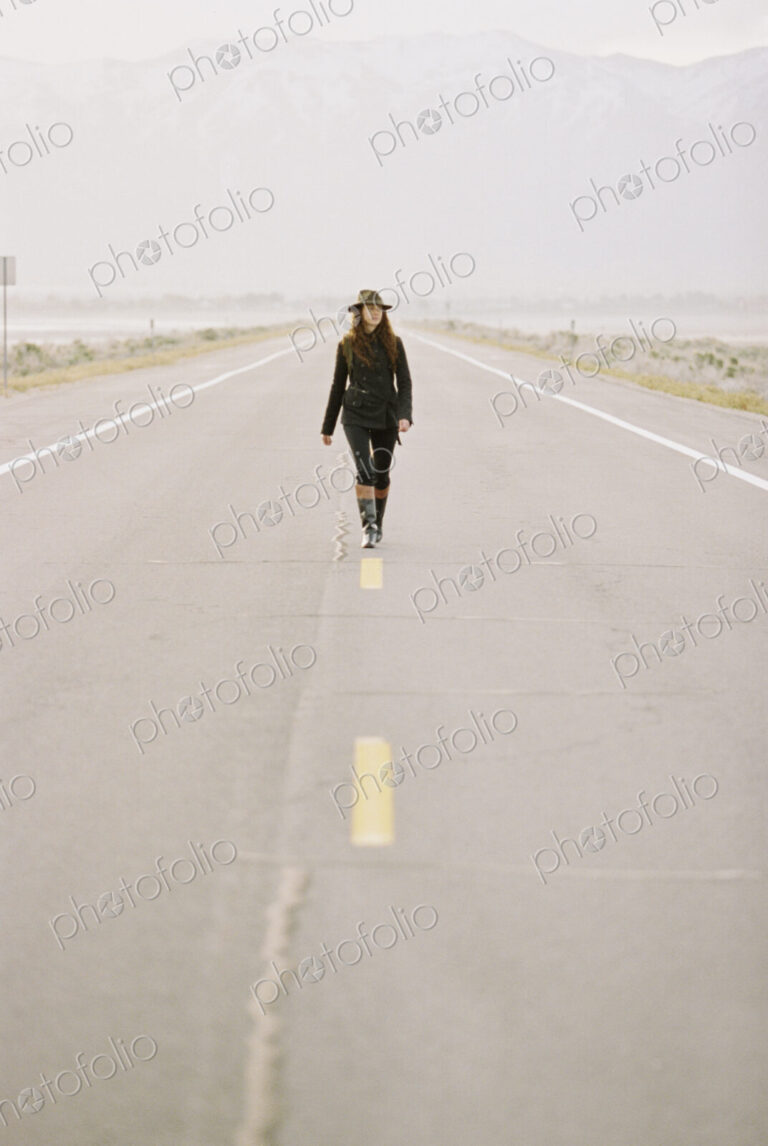 A woman carrying a backpack walking down the centre line of a country road.