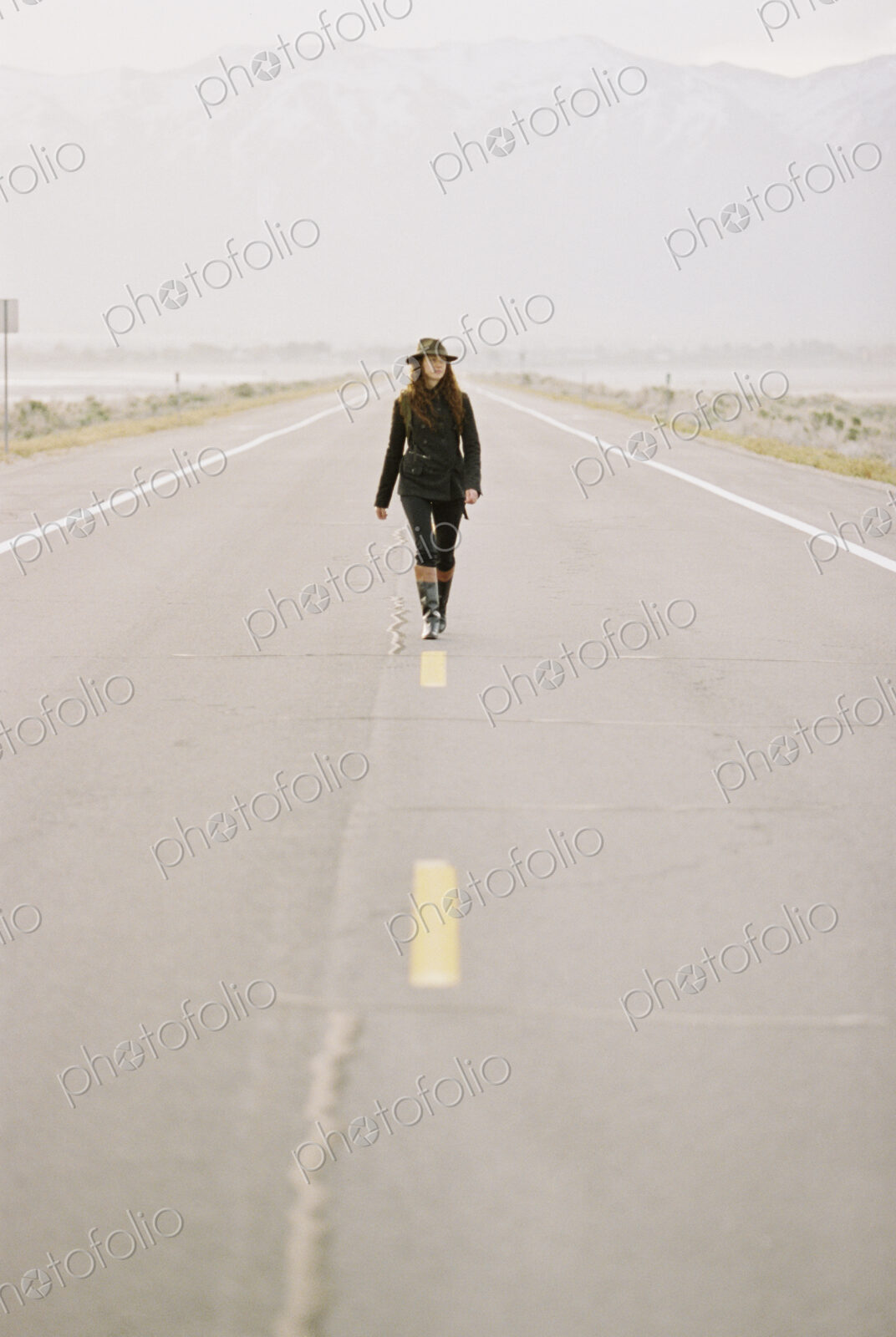 A woman carrying a backpack walking down the centre line of a country road.