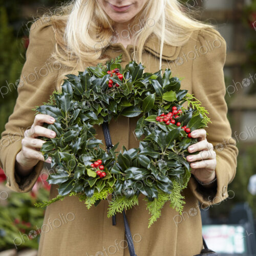 A woman carrying a decorated wreath of holly and everygran leaves. A woman carrying a decorated wreath of holly and everygran leaves.