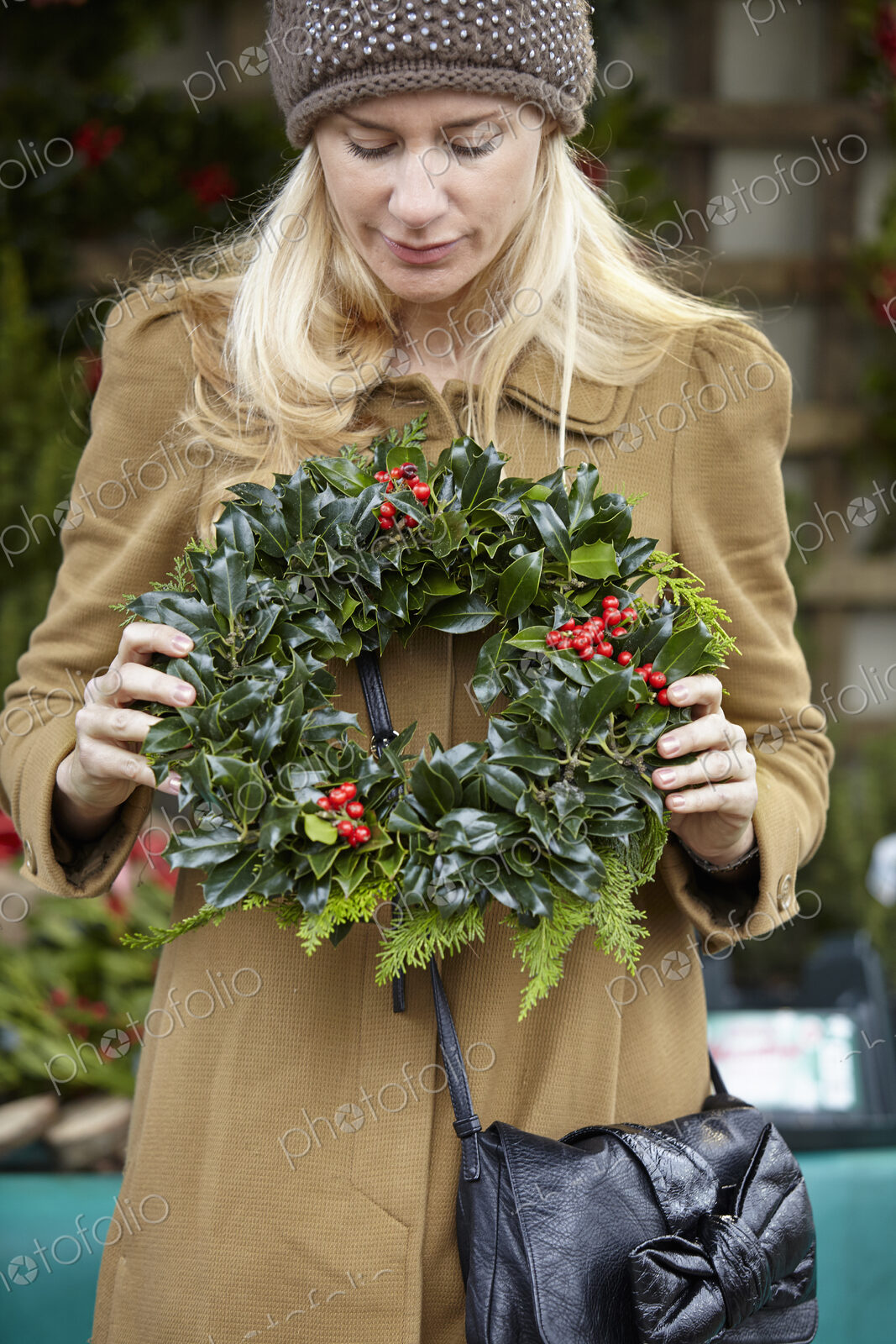 A woman carrying a decorated wreath of holly and everygran leaves.
