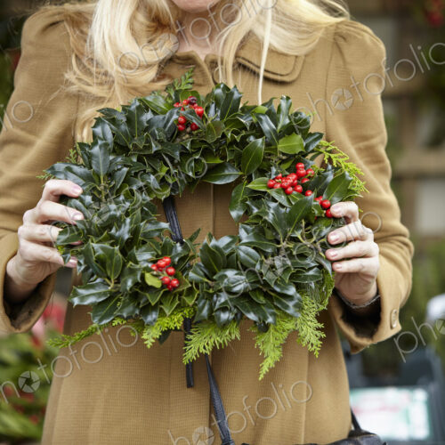 A woman carrying a decorated wreath of holly and everygran leaves. A woman carrying a decorated wreath of holly and everygran leaves.