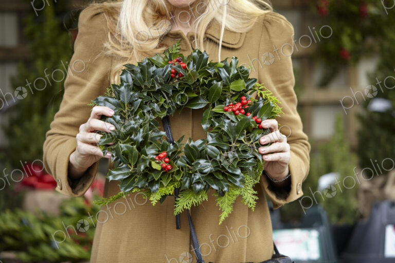 A woman carrying a decorated wreath of holly and everygran leaves.
