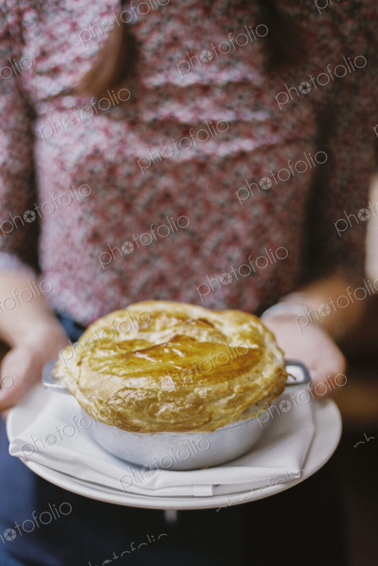 A woman carrying a fresh baked pastry topped pie on a plate.