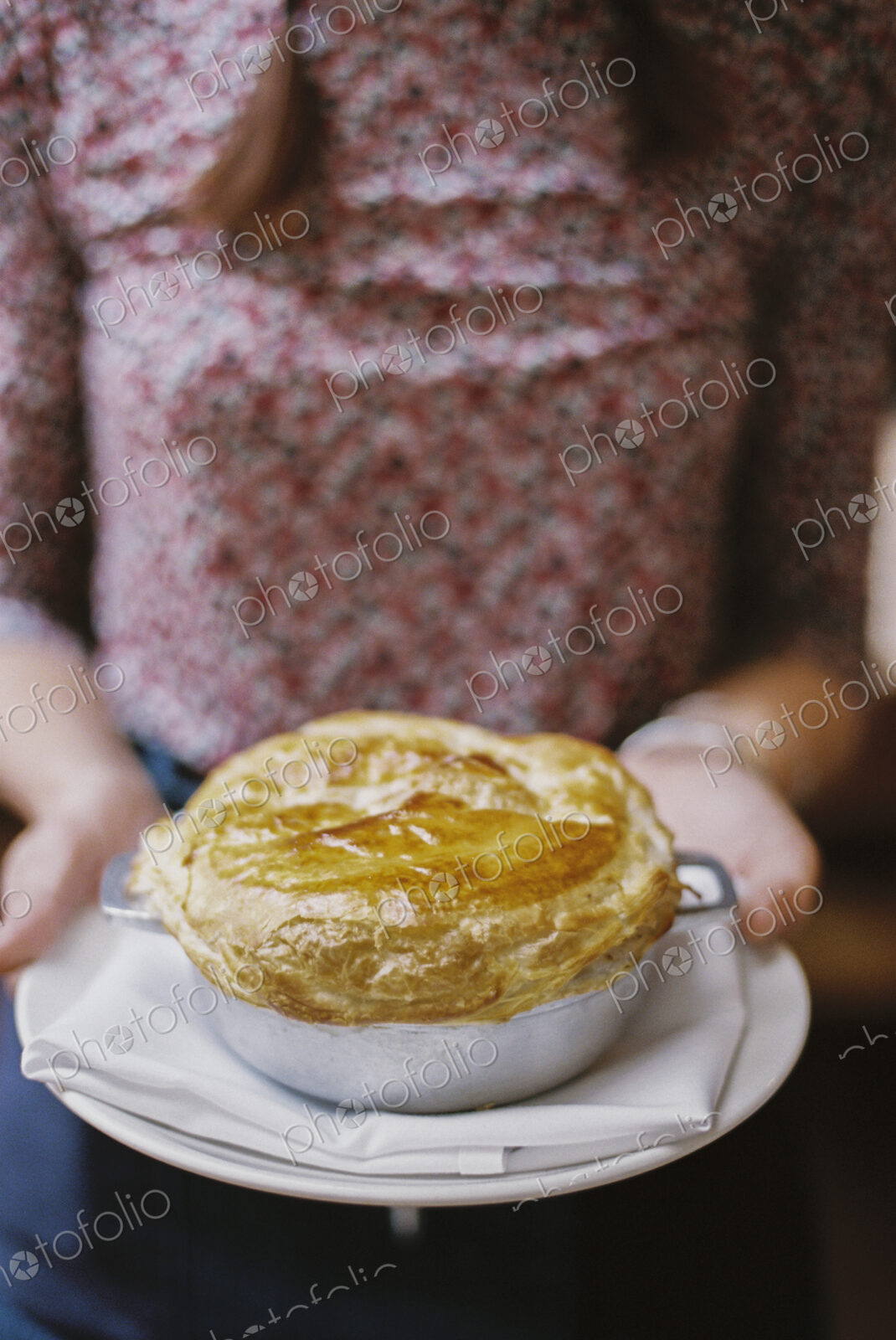 A woman carrying a fresh baked pastry topped pie on a plate.