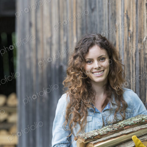 A woman carrying an armful of firewood from the logstore on the farm.