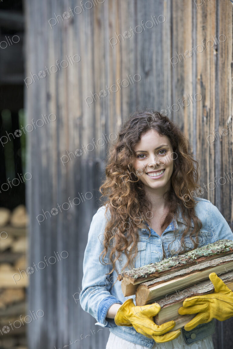 A woman carrying an armful of firewood from the logstore on the farm.