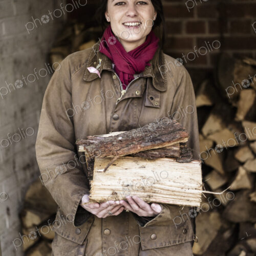 A woman carrying split logs for firewood from a large log store. A woman carrying split logs for firewood from a large log store.