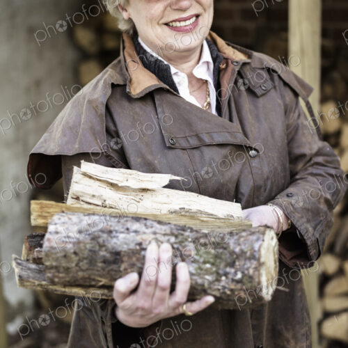 A woman carrying split logs for firewood from a large log store. A woman carrying split logs for firewood from a large log store.