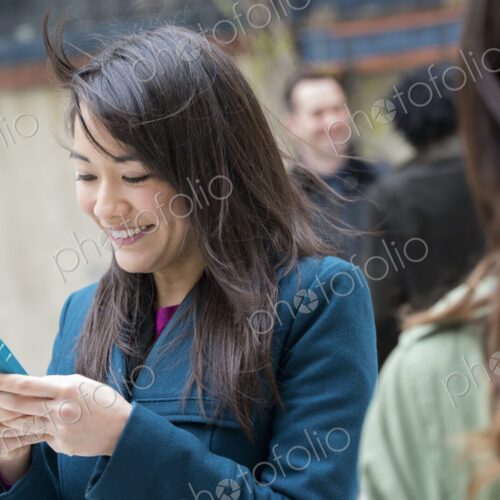 A woman checking her turquoise smart phone, among other people on a city street. A woman checking her turquoise smart phone, among other people on a city street.