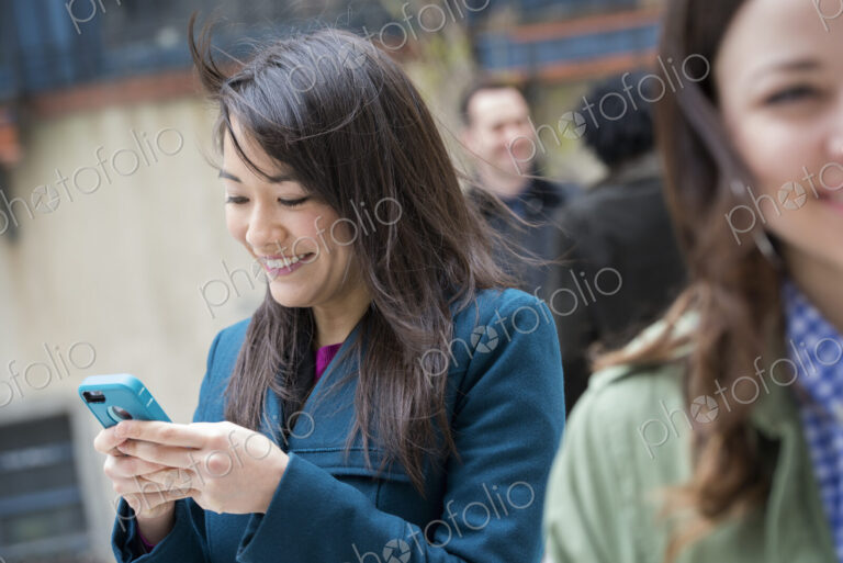 A woman checking her turquoise smart phone, among other people on a city street.