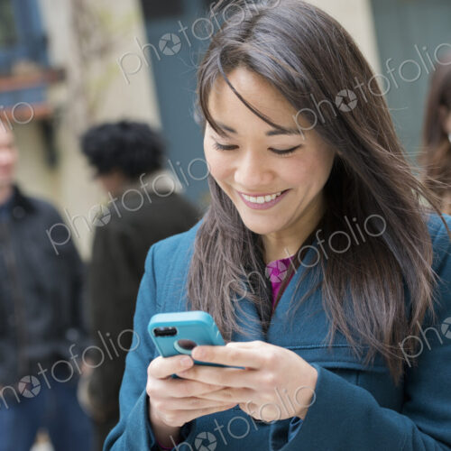 A woman checking her turquoise smart phone, among other people on a city street. A woman checking her turquoise smart phone, among other people on a city street.