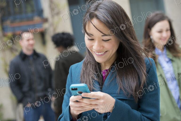 A woman checking her turquoise smart phone, among other people on a city street.
