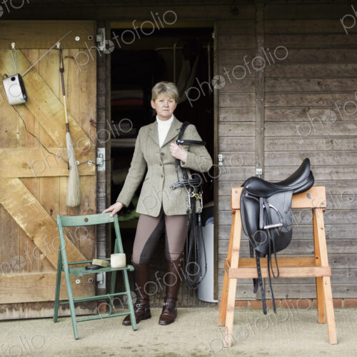 A woman cleaning and preparing tack and saddle, in the courtyard of a riding stable. A woman cleaning and preparing tack and saddle, in the courtyard of a riding stable.