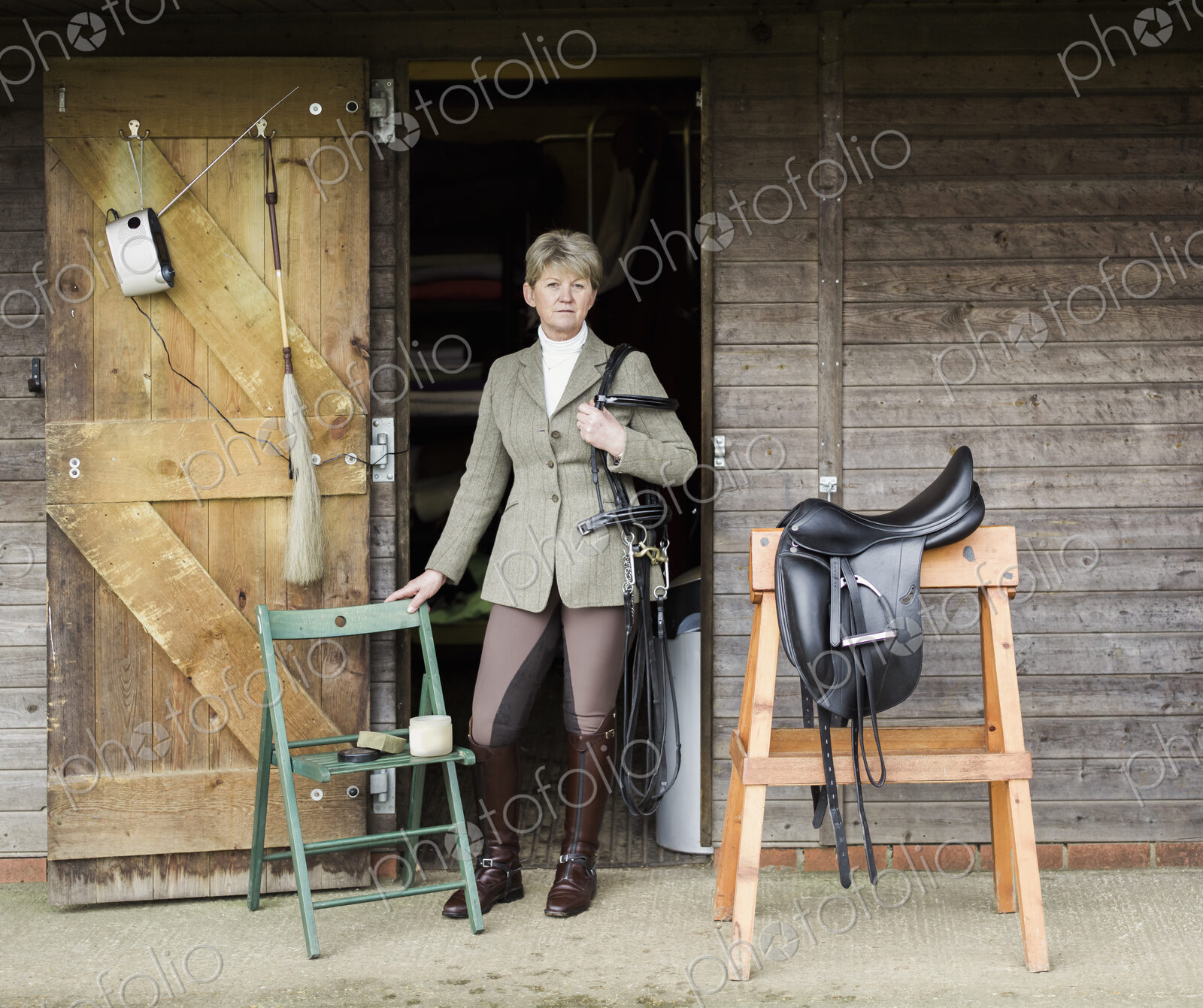 A woman cleaning and preparing tack and saddle, in the courtyard of a riding stable.