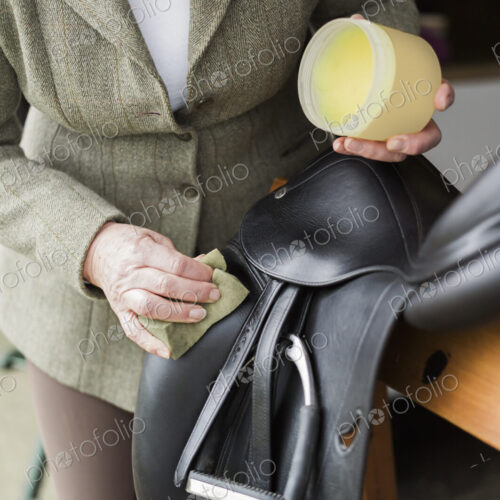 A woman cleaning and preparing tack and saddle, in the courtyard of a riding stable. A woman cleaning and preparing tack and saddle, in the courtyard of a riding stable.