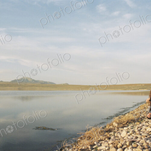 A woman collecting pebbles on the shore of a lake.