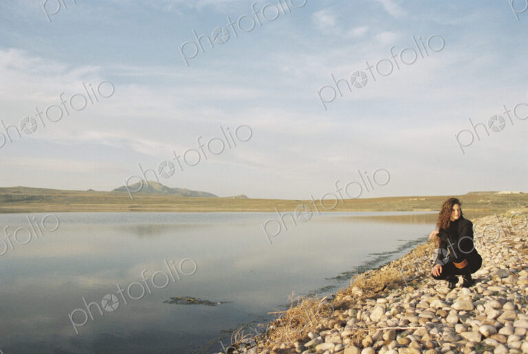 A woman collecting pebbles on the shore of a lake.
