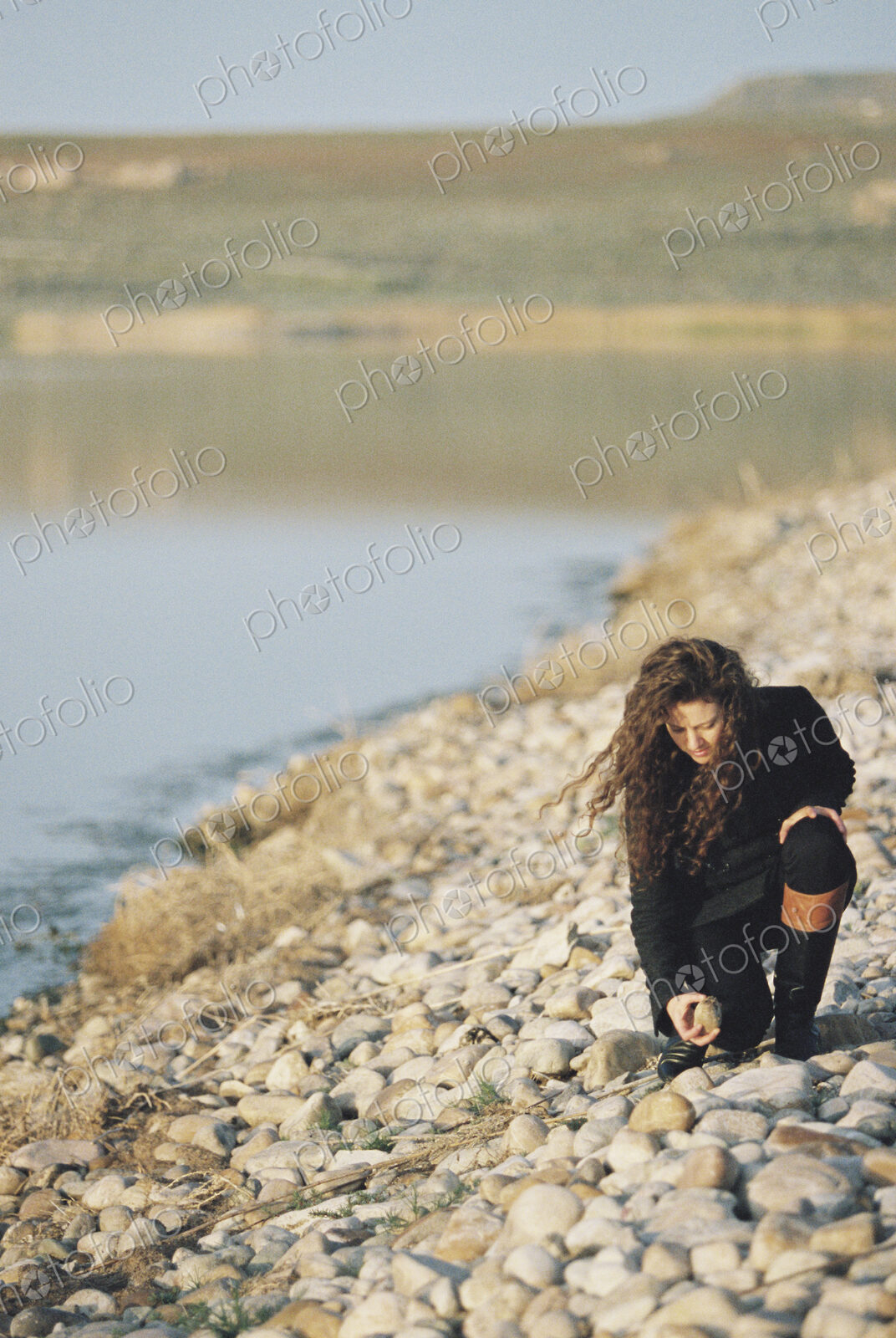 A woman collecting pebbles on the shore of a lake.