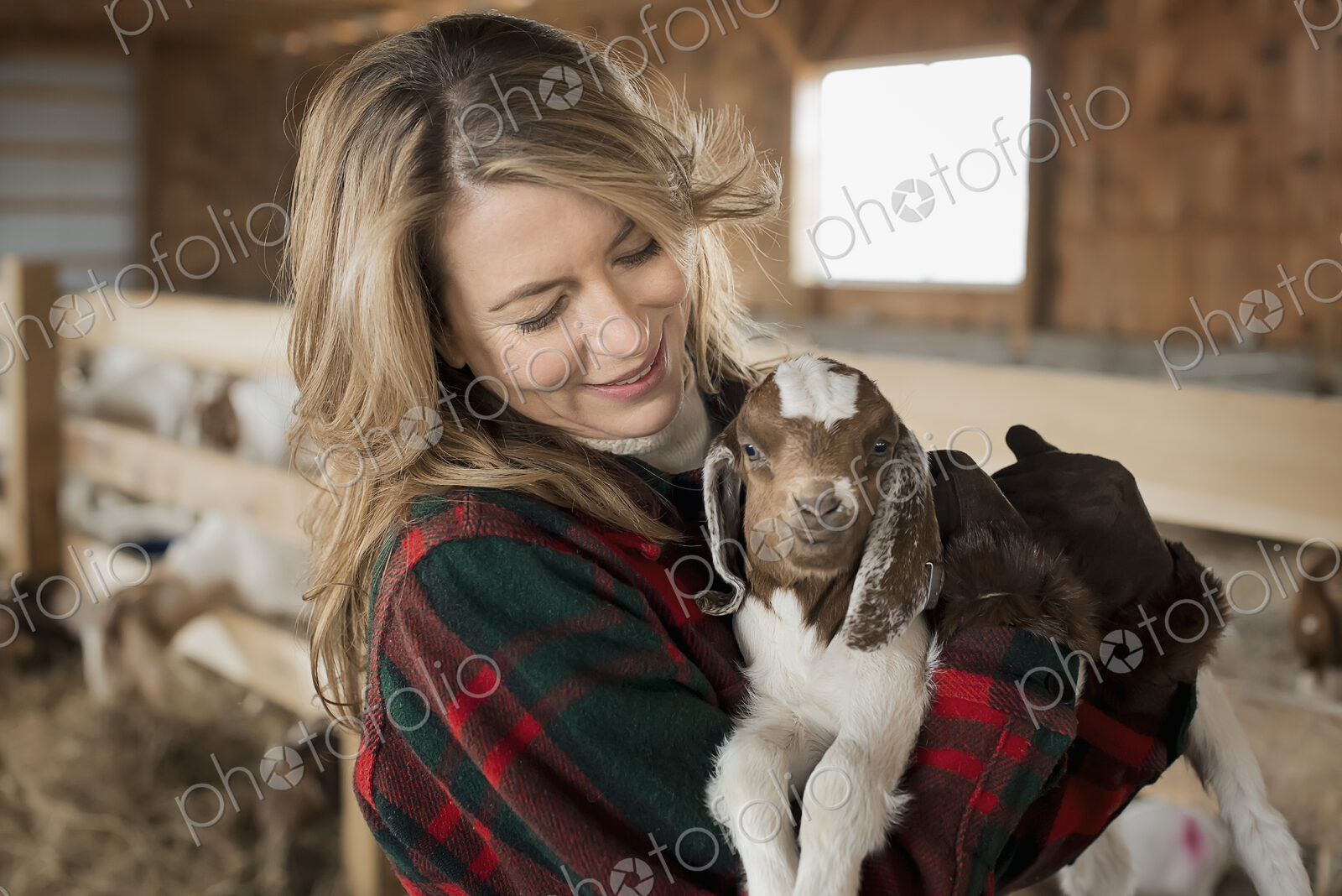 A woman cradling a young goat kid in her arms, on a farm.