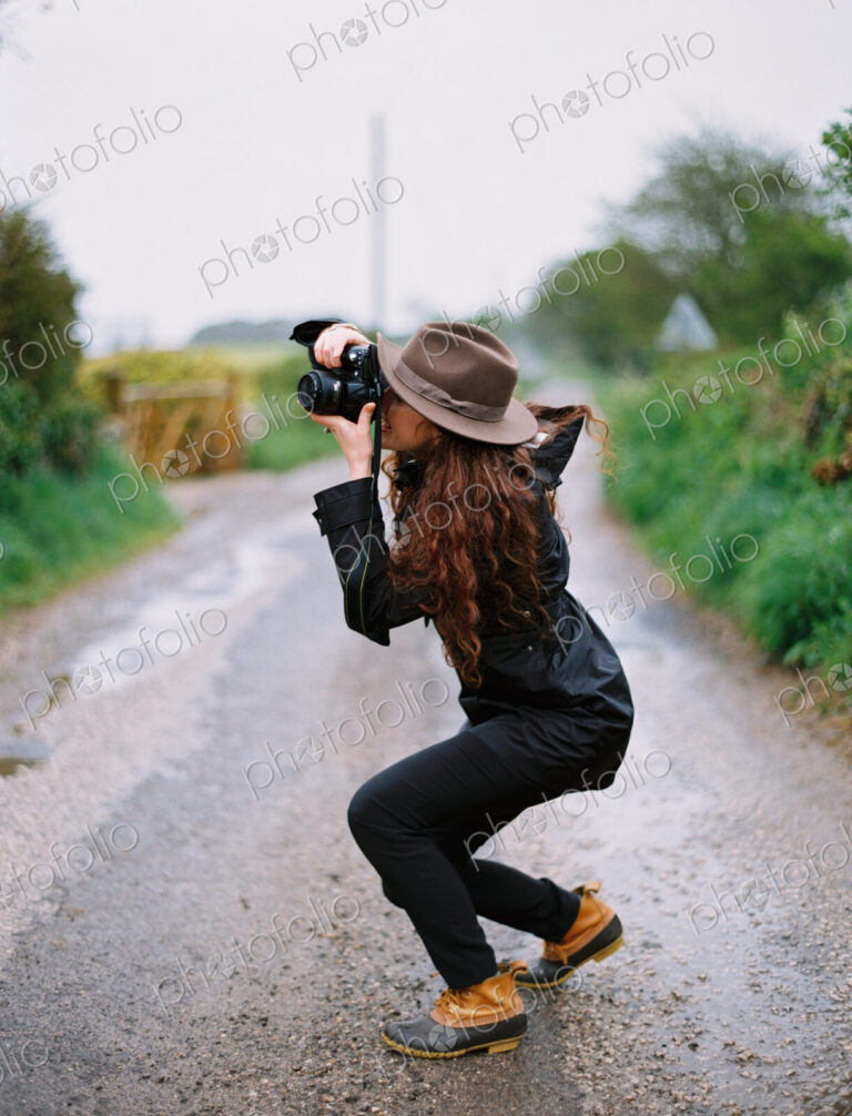 A woman crouching to take a photograph on a country road.
