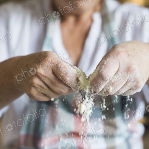 A woman crumbling and sifting white flour and butter, making a crumble topping. Home…