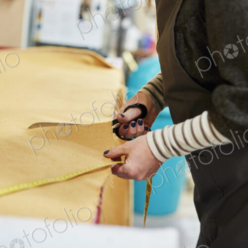 A woman cutting out yellow upholstery fabric on a workbench with a large pair of scissors.